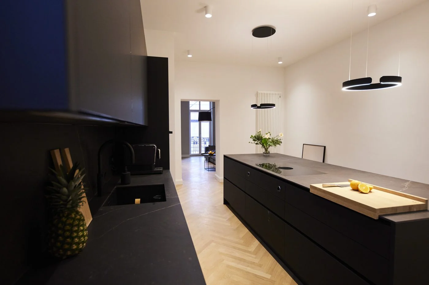 Designerküche im Ostbek 6 mit Fischgrät-Parkett, hängenden Designerleuchten und schwarzer Kochinsel